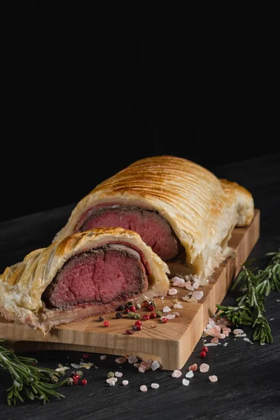 sliced beef wellington on wooden board with spices