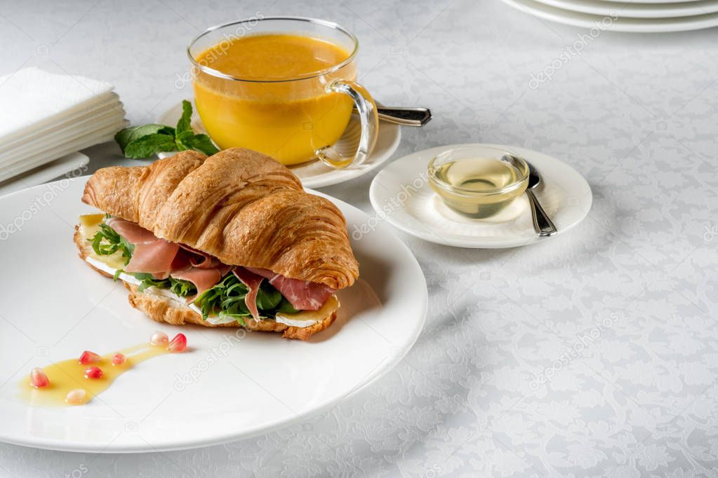 Fresh croissant sandwich served with herbal tea and honey on white table with copy space