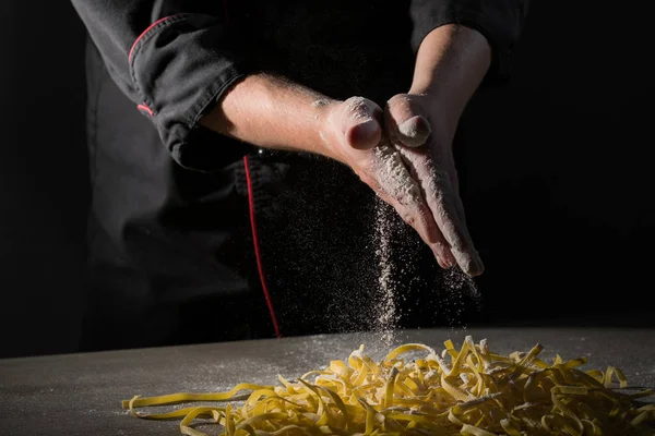 Hands of chef cooking pasta spaghetti powdering by flour on dark black background