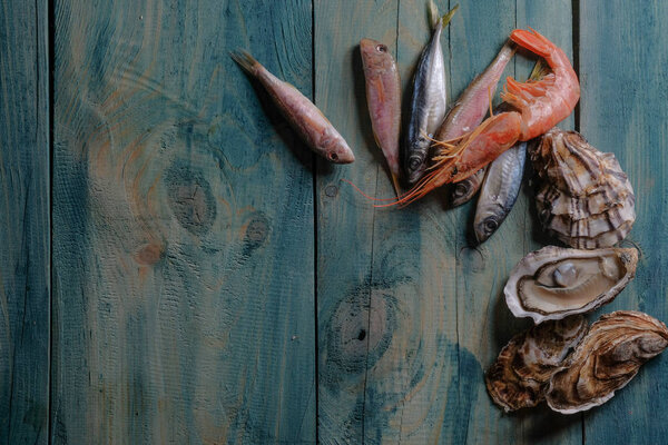 крупным планом набора морепродуктов из свежей рыбы, устриц и креветок на фоне синего деревянного стола
 