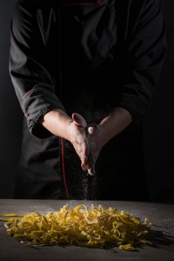 Elinde Şef tarafından un koyu siyah arka plan üzerine spagetti makarna pudralanmaya pişirme