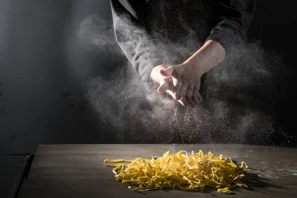 Hands of chef cooking pasta spaghetti powdering by flour on dark black background