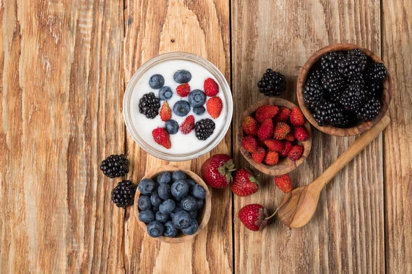 Yoghurt Glas Med Bär Trä Skålar Och Sked Bord Ovanifrån — Stockfoto