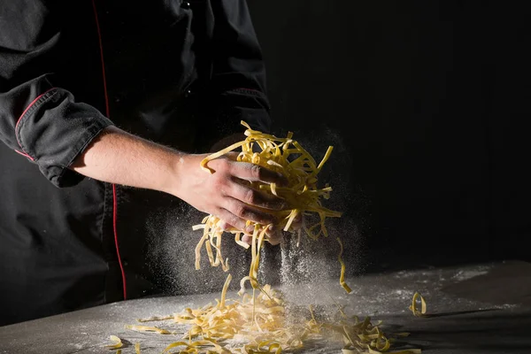 Hands of chef cooking pasta spaghetti powdering by flour on dark black background