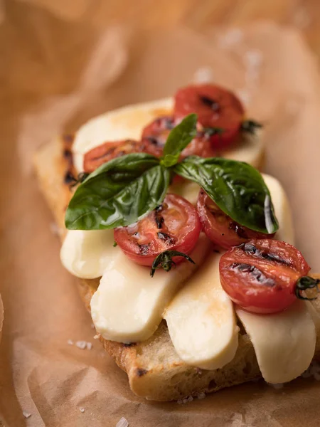 モッツァレラチーズ マッジョーレと羊皮紙紙木製テーブルの上にトマトのおいしいサンドイッチのクローズ アップ  — 無料ストックフォト