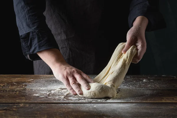 close up of male chef hands preparing dough over wooden background