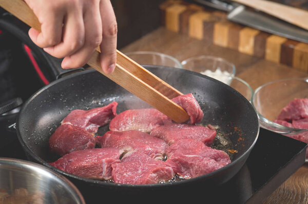 Chef cooks raw meat in a frying pan for cooking a recipe with fried meat