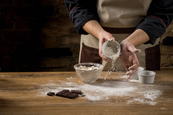 Chef cooking cake in glass bowl with dough, flour and ingredients wood background