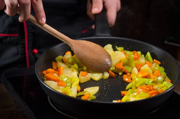 Chef cooks vegetables in a frying pan for cooking a recipe
