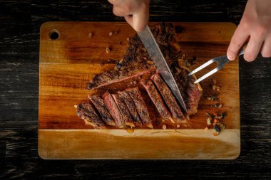 Elinde bıçakla ve baharat ahşap tahta arka plan ile ızgara et oyma erkek eller   
