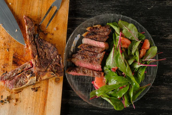 carving grilled meat with spices,knife and fork on wooden board background