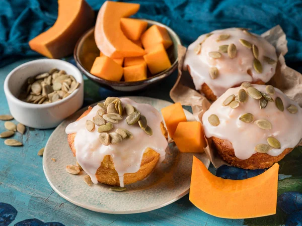 close-up of homemade sweet pumpkin cupcakes with seeds near blue scarf on wooden background
