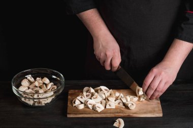 birlikte cam kaseye koyarak ahşap tahta arka plan üzerinde bıçak ve kesme mantar holding erkek Şef eller Close-Up