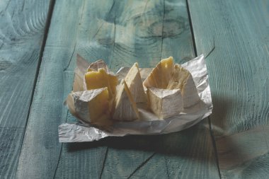 Mavi ahşap masa arka plan üzerinde beyaz kağıda lezzetli Camembert peyniri kesme yakın çekim 