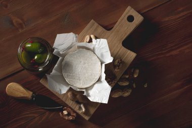 brie peyniri, bıçak, otlar ve kavanoz zeytin ve capperi ahşap masa üzerinde düz lay