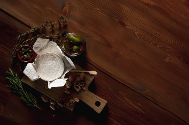 brie peyniri, bıçak, otlar ve kavanoz zeytin ve capperi ahşap masa üzerinde düz lay