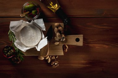 brie peyniri, bıçak, otlar ve kavanoz zeytin ve capperi ahşap masa üzerinde düz lay