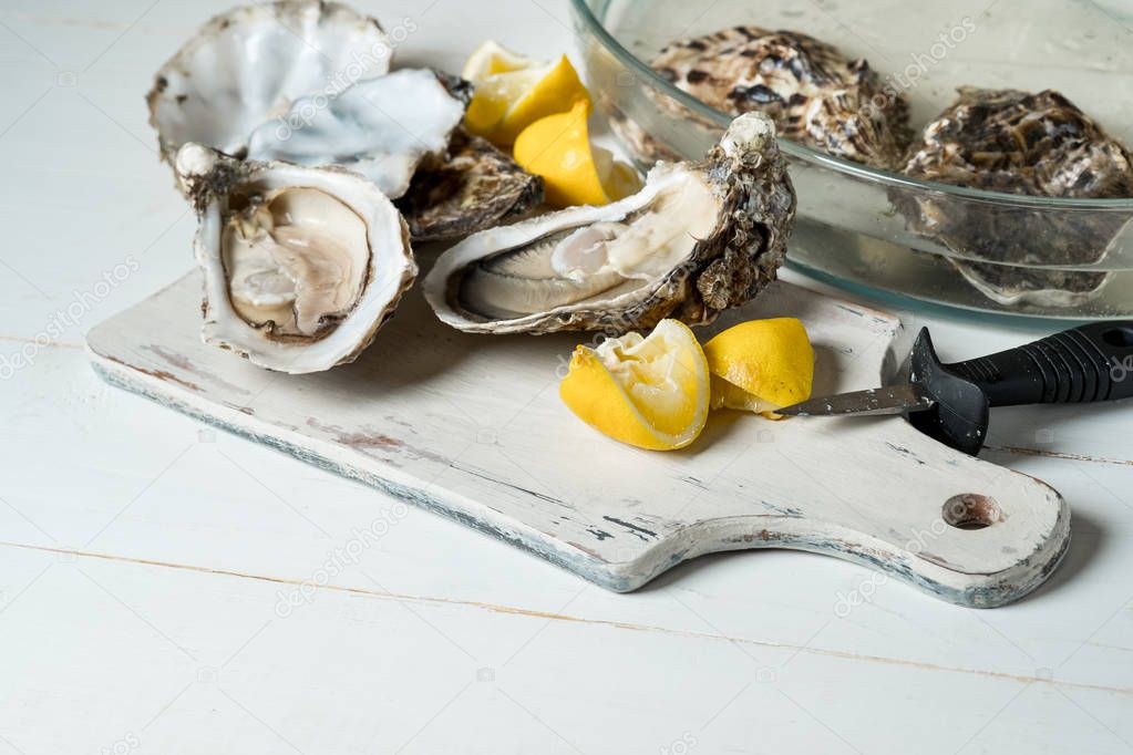 fresh raw oysters with lemon slices on wooden board with knife and bowl on white table