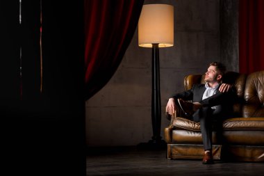 Lamba yakınındaki deri kanepede oturan takım elbiseli genç işadamı