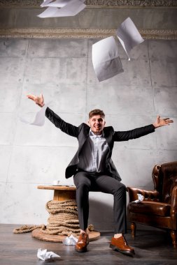 Tahta masada oturan ve kağıtları çöpe kızgın genç işadamı