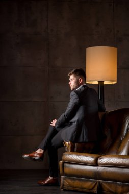 Lamba yakınındaki deri kanepede oturan takım elbiseli genç işadamı