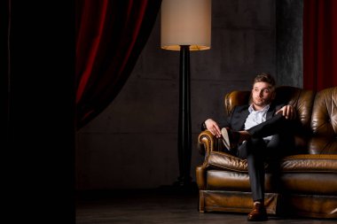 Lamba yakınındaki deri kanepede oturan takım elbiseli genç işadamı