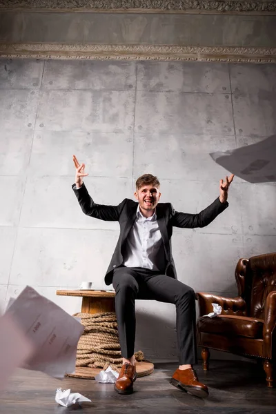 Young angry businessman sitting on wooden table and throwing away papers
