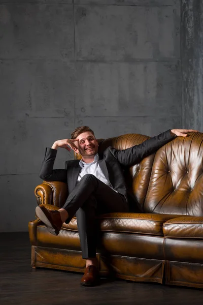 Young happy businessman in suit sitting on leather sofa