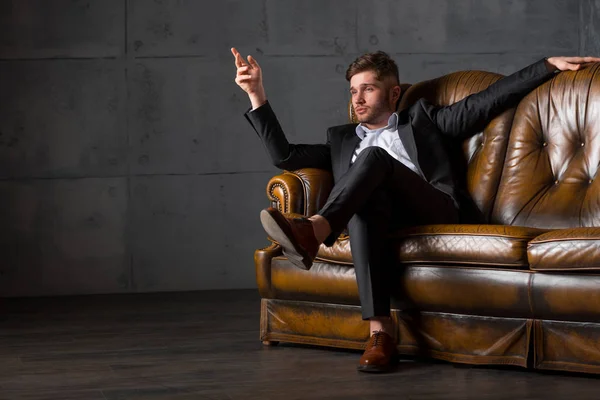 Young tired businessman in suit sitting on leather sofa