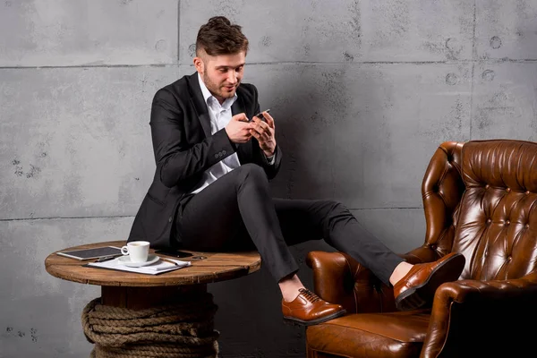 Young happy man in suit sitting on wooden table using smartphone