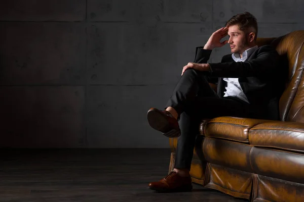 Young tired businessman in suit sitting on leather sofa