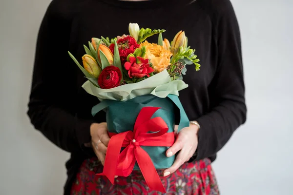 Female florist holding stylish bouquet of red and orange flowers