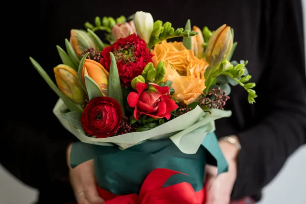 Female florist holding stylish bouquet of red and orange flowers