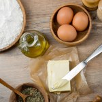 Wirydarz-do góry fotografia świeżych jaj w drewnianej tablicy z mąka, oliwa z oliwek, przyprawy i masło na tle tabeli