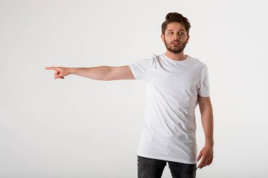 gri arka plan üzerinde Beyaz gömlekli bir eliyle işaret eden genç sakallı adam portresi 