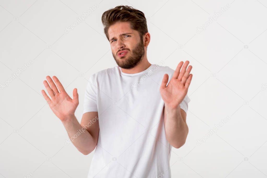 portrait of young bearded disgusted man gesture in white shirt on grey background 