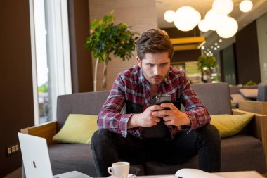 Mobil kapalı gri kanepe arka plan üzerinde kullanarak ekose gömlekli genç sakallı adam portresi 