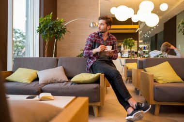 Ekose gömlek içki kahve beyaz fincan gri kanepe arka plan üzerinde kapalı genç sakallı adam portresi