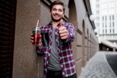 ekose gömlekli arka başparmak gösterilmesini bina üzerinde taze meyve suyu tutan genç sakallı adam portresi