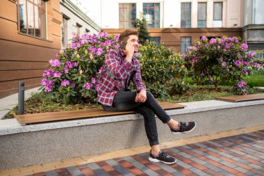 Mobil açık arka plan üzerinde pembe çiçekli kullanarak ekose gömlekli genç sakallı adam portresi