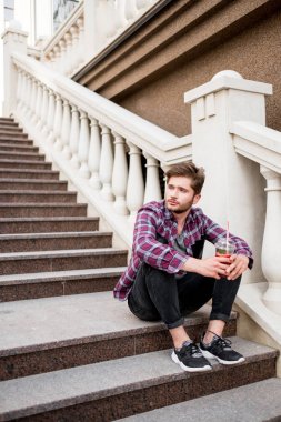 ekose gömlekli merdivenlerde oturan taze meyve suyu tutan genç sakallı adam portresi 