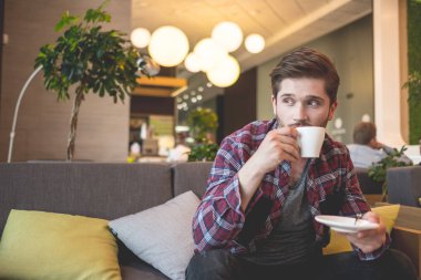 Ekose gömlek beyaz fincan kahve gri kanepe arka plan üzerinde kapalı tutan genç sakallı adam portresi 