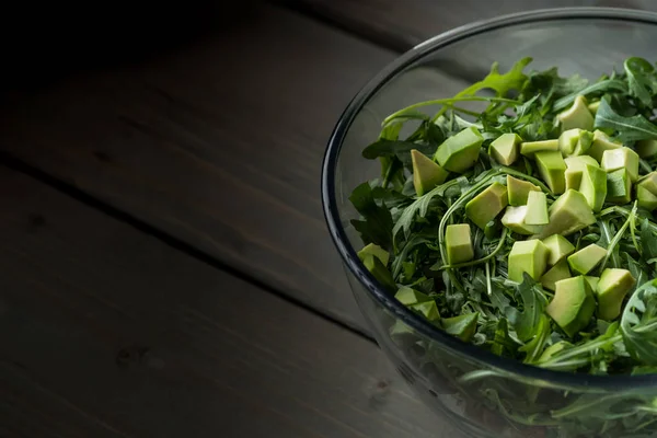 在木桌上的玻璃碗里用鳄梨和芝麻菜做健康新鲜绿色沙拉的特写照片 — 图库照片