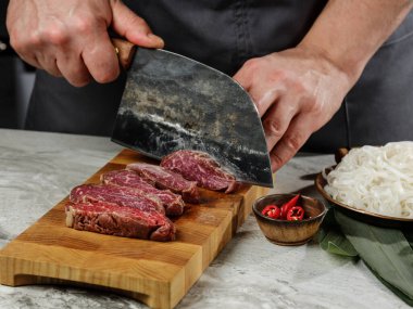 Asya yemekleri - Biftekli pirinç eriştesi ve beyaz masa arkasında mango sosu malzemesi..