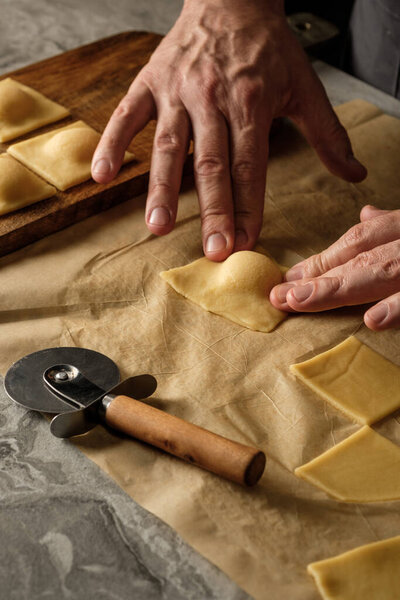 Cooking ravioli pasta with ricotta cheese handmade with cook hands on wooden table background.