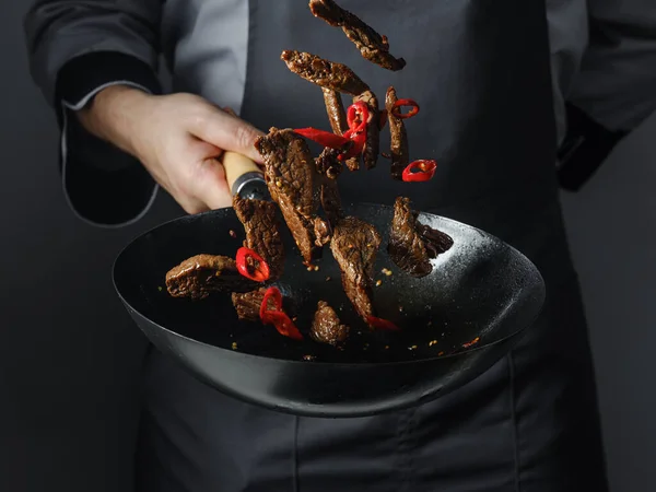 Cooking in wok pan - sliced beef meat and chilli pepper on black background, professional restaurant and hotel service food concept.