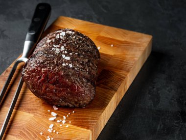 Izgarada biftek fileto pişiriyorum. Siyah arka planda tuz ve biber ve fotokopi uzay metni. Yemek tarifi konsepti