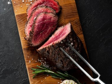 Izgara sulu biftek seçilmiş mermer et dilimler üzerinde tahta masa üzerinde siyah arka plan halk ve bıçak ile kesilmiş