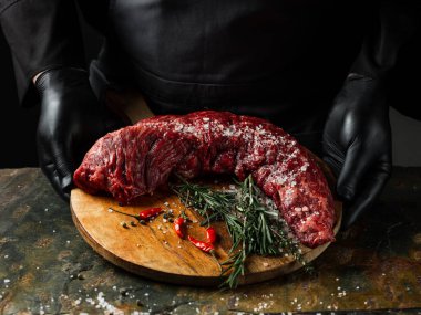 Biberli büyük bıçaklı kasapla biftek fileto eti, tuz, taş masa üzerinde otlar arka planda. Düz görünüm, genel görünüm