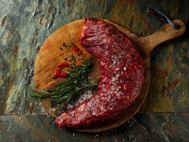 Biberli büyük bıçaklı kasapla biftek fileto eti, tuz, taş masa üzerinde otlar arka planda. Düz görünüm, genel görünüm